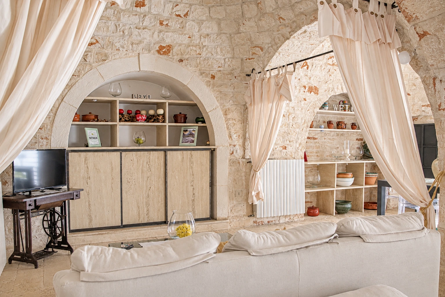 La sala del trullo: gli archi in pietra, le tende chiare e il divano bianco