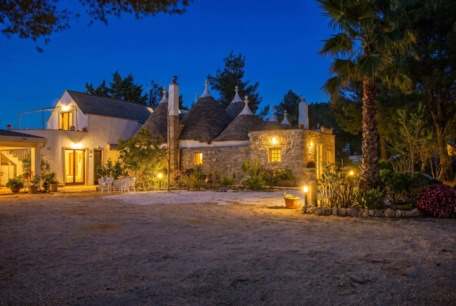 Masseria Battaglini in the evening: lit windows and trulli roofs against a blue sky