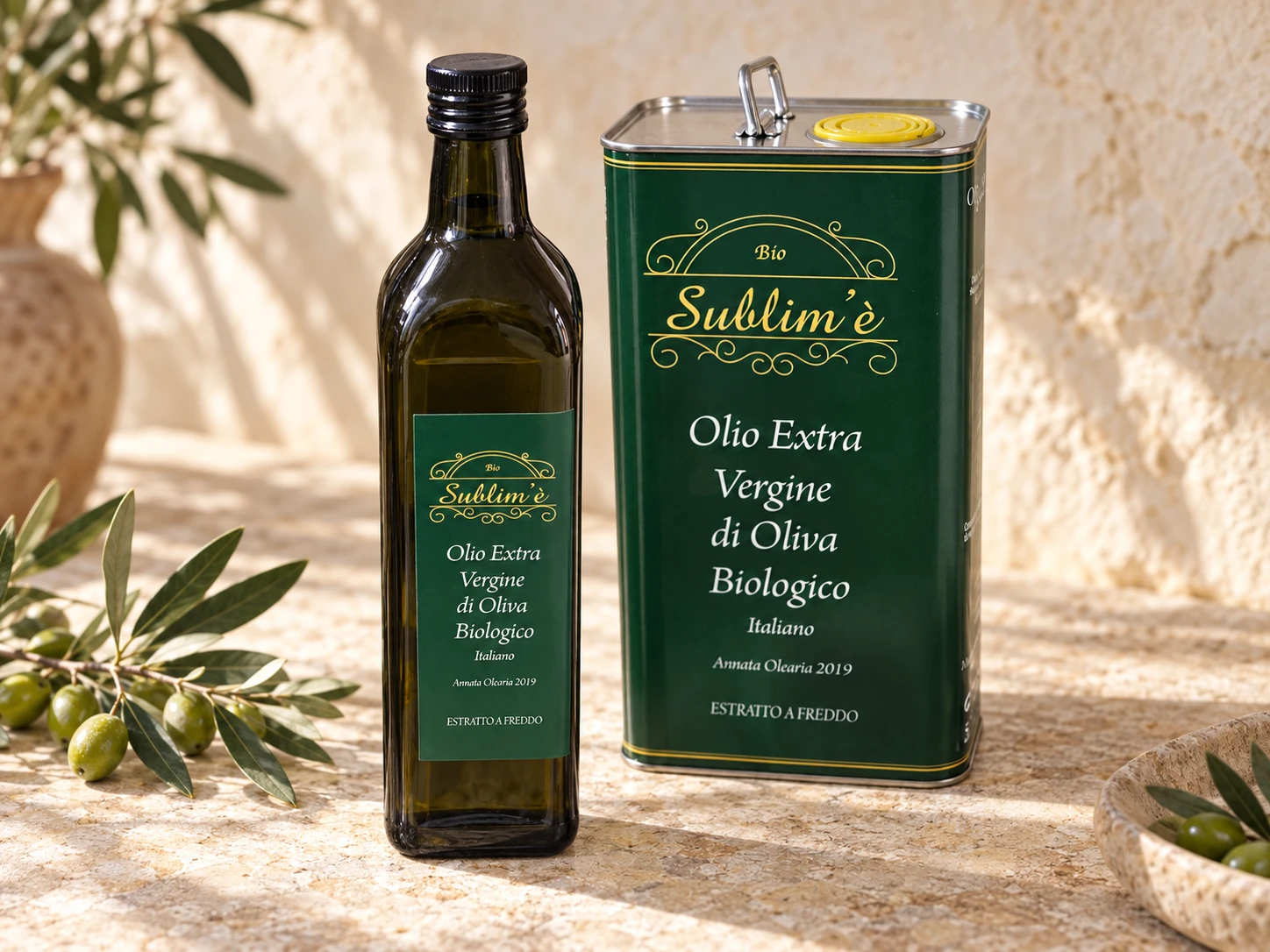 Bottiglia e tanichetta di olio biologico Sublim’è su pietra chiara, accanto a rami di ulivo