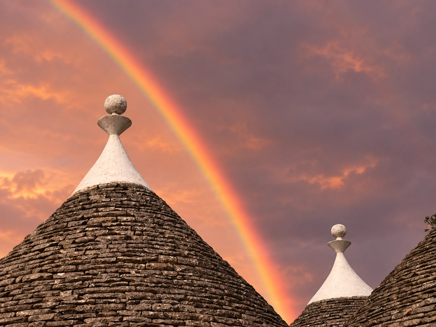 A rainbow crosses the pink sky above the trulli roofs